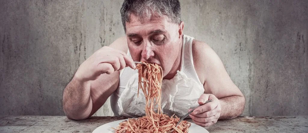 pessoa sentada na mesa comendo com compulsão alimentar